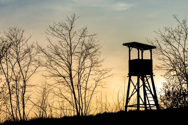 stock image Silhouette of a hunting tower and trees on a glade during the sunset.