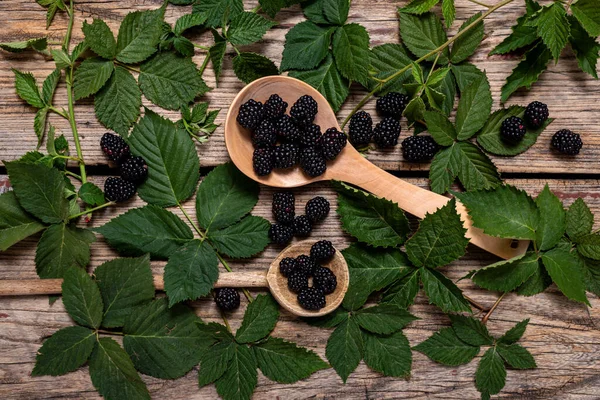 Köy arka planında yeşil yapraklı iki tahta kepçeyle taze böğürtlen. Düz yatış, üst görünüm.