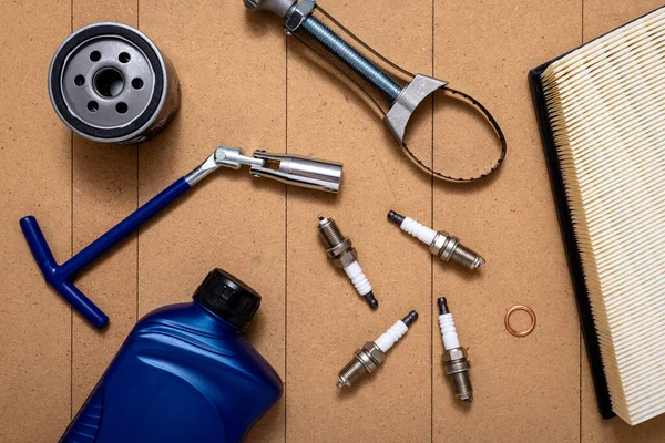 Bottle of motor oil, oil filter, air filter, sparking plugs, spark plug key and oil filter wrench on wooden background. Car repairing service concept.