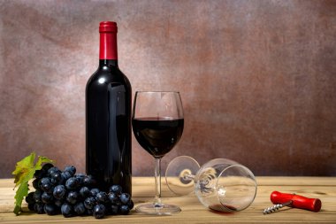 Şarap şişesi ve kırmızı şarap kadehi, tirbuşon ve ahşap masada taze üzümler. Seçici odak.