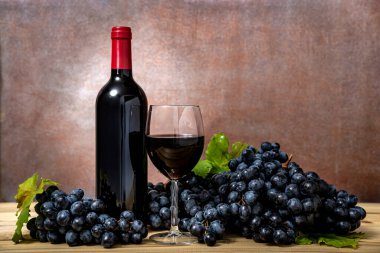 Şarap şişesi ve kırmızı şarap kadehi ve ahşap masada taze üzümler. Seçici odak.