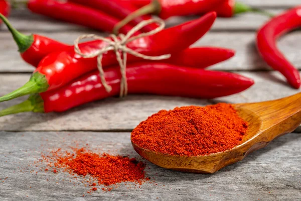 Değirmende öğütülmüş biberli ahşap kaşık ve eski masada taze kırmızı biber. Seçici odak.