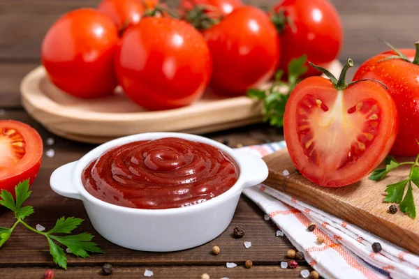 stock image Ceramic bowl of ketchup or tomato sauce, spices and fresh tomatoes on wooden table. Selective focus.