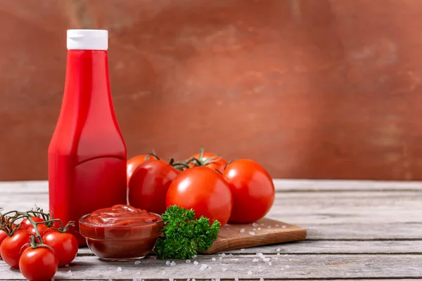 Plastik şişe ve cam kase ketçap veya domates sosu, baharatlar ve ahşap masada taze domatesler. Seçici odak.