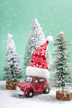Tahta bir masada kar yağarken çatıda Noel Baba şapkalı kırmızı oyuncak araba. Kış ve Noel konsepti.
