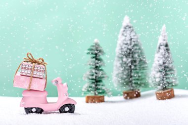 Kar yağarken köknar ağaçlarının yanında Noel hediyeleri olan pembe bir motosiklet. Noel ve Yeni Yıl kutlaması kavramı.