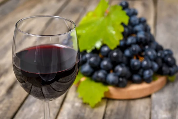 Wine glass with red wine and fresh grapes on wooden table with copy space for text. Selective focus.