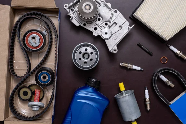 Repair kit for replacing the timing belt in a open cardboard box and cooling pump, sparking plugs and filters on a working table.