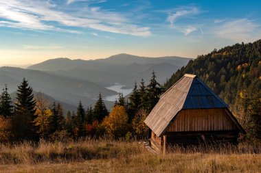 Sırbistan 'ın Zmajevac, Tara Dağı ve Zmajevac perspektifinde gün batımından önce küçük ahşap kulübe ve Zaovine gölünün güzel manzarası.