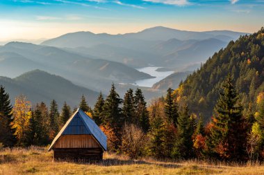 Sırbistan 'daki Zmajevac, Tara Dağı ve Zmajevac perspektifinde sonbaharda günbatımından önce küçük ahşap kulübe ve Zaovine gölünün güzel manzarası.