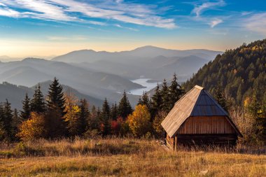 Sırbistan 'daki Zmajevac, Tara Dağı ve Zmajevac perspektifinde sonbaharda günbatımından önce küçük ahşap kulübe ve Zaovine gölünün güzel manzarası.