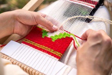 El dokuma tezgahında dokuma iğnesi kullanan bir kadın eli. Seçici odak.