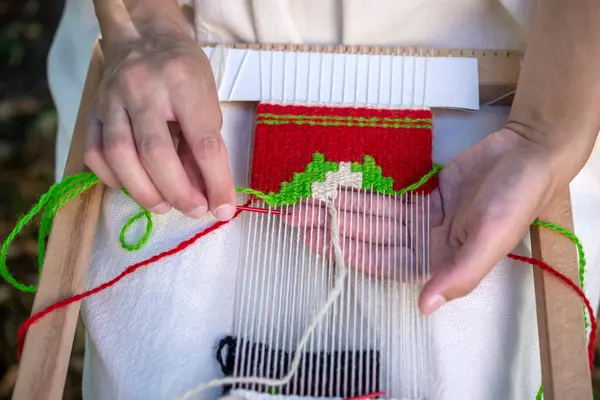 El dokuma tezgahında dokuma iğnesi kullanan bir kadın eli. Seçici odak.