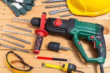 Ahşap bir masanın üzerinde bir takım aksesuar ve koruyucu ekipmanla çekiç matkabı. Seçici odak.
