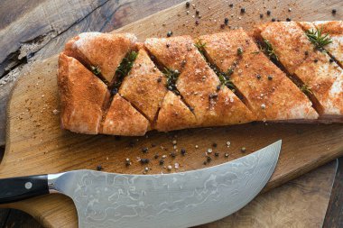 Ağaç kesme tahtasında çiğ domuz eti, baharatlar, tuz, biber, biberiye ve bir bıçak.