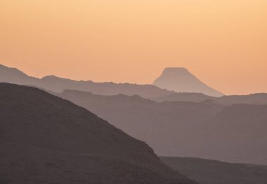 Sıcak bir günbatımı uzak dağların siluetlerini aydınlatır. Altın renkler huzurlu ve huzurlu bir çöl atmosferi yaratır.