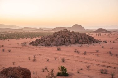 Namibya Çölü, binlerce yıldır doğal süreçler tarafından şekillendirilen dağınık kahverengi taşlara ve engebeli kaya oluşumlarına ev sahipliği yapar. Bu özellikler etrafındaki altın kumlarla keskin bir tezat oluşturarak kendine özgü bir çöl manzarası yaratır.