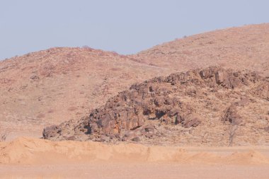 Namibya Çölü, binlerce yıldır doğal süreçler tarafından şekillendirilen dağınık kahverengi taşlara ve engebeli kaya oluşumlarına ev sahipliği yapar. Bu özellikler etrafındaki altın kumlarla keskin bir tezat oluşturarak kendine özgü bir çöl manzarası yaratır.