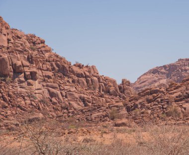 Namibya Çölü, binlerce yıldır doğal süreçler tarafından şekillendirilen dağınık kahverengi taşlara ve engebeli kaya oluşumlarına ev sahipliği yapar. Bu özellikler etrafındaki altın kumlarla keskin bir tezat oluşturarak kendine özgü bir çöl manzarası yaratır.