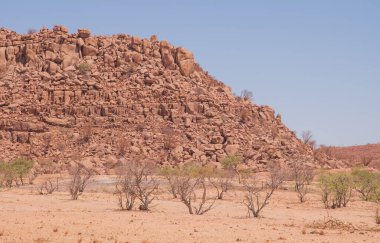 Namibya Çölü, binlerce yıldır doğal süreçler tarafından şekillendirilen dağınık kahverengi taşlara ve engebeli kaya oluşumlarına ev sahipliği yapar. Bu özellikler etrafındaki altın kumlarla keskin bir tezat oluşturarak kendine özgü bir çöl manzarası yaratır.