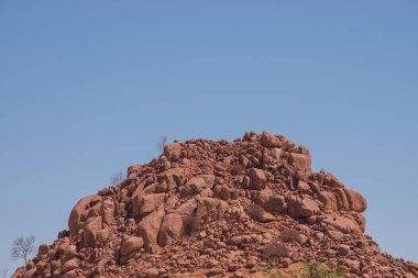 Namibya Çölü, binlerce yıldır doğal süreçler tarafından şekillendirilen dağınık kahverengi taşlara ve engebeli kaya oluşumlarına ev sahipliği yapar. Bu özellikler etrafındaki altın kumlarla keskin bir tezat oluşturarak kendine özgü bir çöl manzarası yaratır.