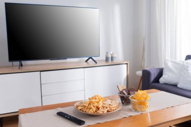 Arkaplanda boş TV ekranı olan ahşap masada atıştırmalık.