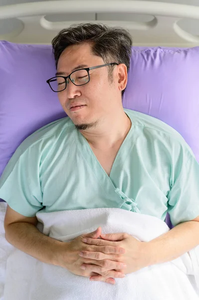 Asian man lying in bed sleeping in hospital ward