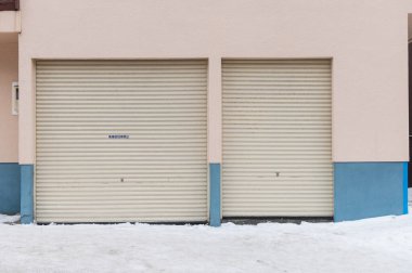 Yerde kar olan bir binanın iki kapalı garaj kapısı.