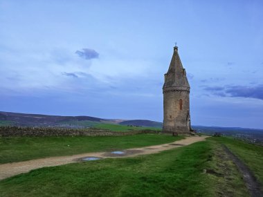 Bu çarpıcı görüntü, İngiltere 'nin Ashton-under-Lyne kentindeki tarihi Hartshead Pike Kulesi' ni günbatımının ılık renklerinde yakalar. 2. Sınıf simgesi olan kule manzaralı bir tepenin tepesinde duruyor. Büyük Manchester ve B 'nin nefes kesici manzaralarını sunuyor.