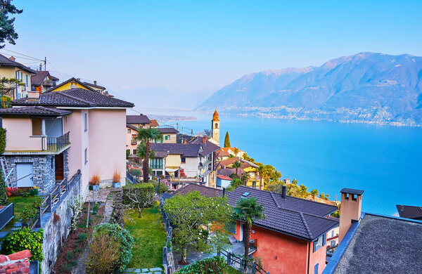The beautiful mountain village of Ronco sopra Ascona with small houses, green gardens, clocktower of San Martino Church and blue Lake Maggiore in background, Switzerland