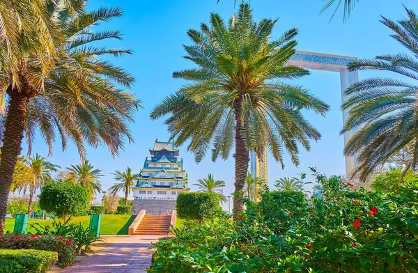 stock image DUBAI, UAE - MARCH 6, 2020: The lush palms and green bushes in Zabeel Park with Dubai Frame and mini Osaka Castle in the background, on March 6 in Dubai