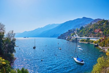 Maggiore Gölü 'nde güzel bir liman demirli yatlar, küçük botlar ve botlarla çevrili mavi puslu dağlarla çevrili, Ascona, İsviçre
