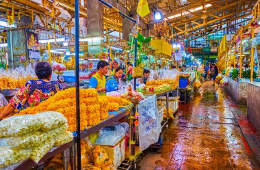 BANGKOK, THAILAND - APRIL 23, 2019: The alley in Pak Khlong Talat Flower Market with sellers making flower compositions, on April 23 in Bangkok clipart