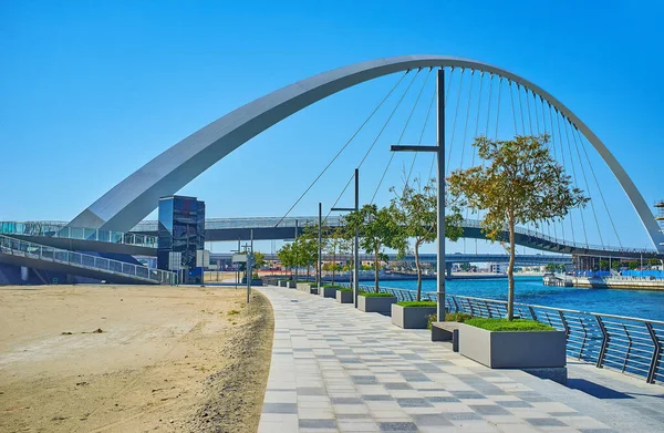 stock image The curved alley with green trees along Dubai Water Canal with a view on the modern pedestrian Tolerance Bridge, Dubai, UAE