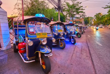 CHIANG MAI, THAILAND - MAY 3, 2019: The line of parked tuk tuks by the road at sunset, on May 3 in Chiang Mai