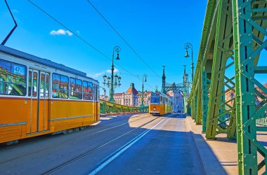 Fast morning traffic on historic Liberty Bridge with a view on riding yellow vintage trams, Budapest, Hungary