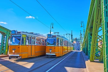 The vintage yellow trams on historic green Liberty Bridge across Danube river, Budapest, Hungary