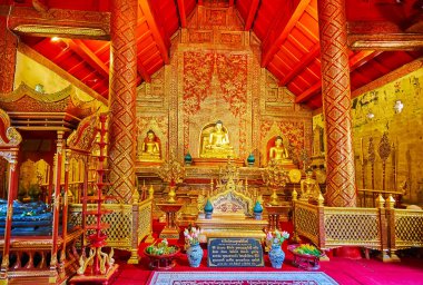 CHIANG MAI, THAILAND - MAY 3, 2019: Interior of Viharn Lai Kham of Wat Phra Singh temple with devotees, praying at the altar and rich red-golden decorations, on May 3 in Chiang Mai