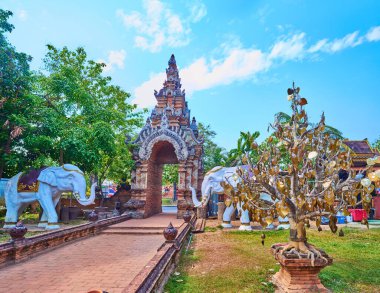The grounds of Wat Lok Moli with a view on its medieval brick gate, elephant statues and golden Bodhi Tree, Chiang Mai, Thailand