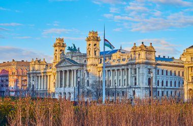 The garden beds on Lajos Kossuth Square with a view on Ethnographic Museum building with stone towers, colonnade, sculptured pediment and bronze quadriga, Budapest, Hungary