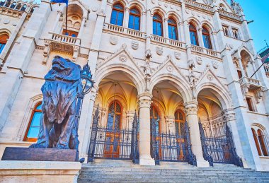 The lion guardian statue in front of the facade of Hungarian Parliament, decorated in Neo-Gothic style, Budapest, Hungary