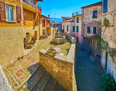 The medieval Piazza Rusciett in Castello with preserved living houses, small drinking fountain and plants in pots, Valsolda, Italy
