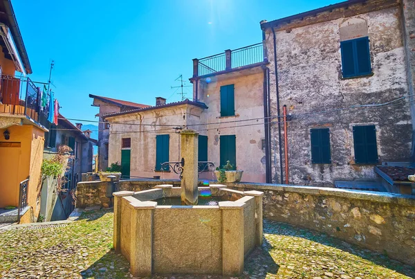 stock image The medieval stone fountain and historic housing on Piazza Rusciett, Castello, Valsolda, Italy