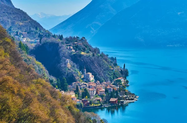 stock image Colored houses of San Mamete and the medieval church at the mountain foot on the bank of Lake Lugano, Valsolda, Switzerland