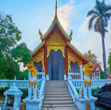 The Viharn of Wat Pan Ping decorated with carved bargeboards, gilt patterns on gable end and the statues of Chinthe lions on the foreground, Chiang Mai, Thailand