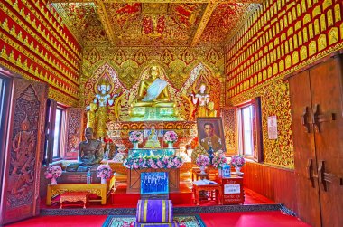 CHIANG MAI, THAILAND - MAY 3, 2019: Interior of the shrine-library of Wat Buppharam, richly decorated with gilt stucco ornaments, statues of bhikkhu monk and golden Buddha, Chiang Mai