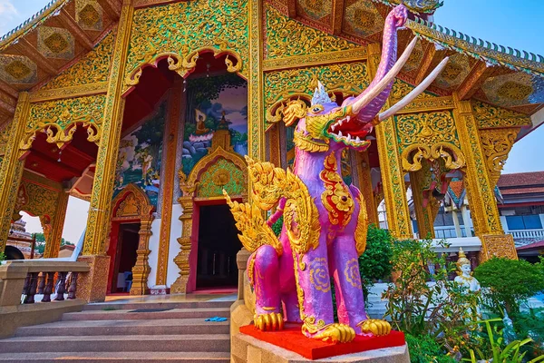 The purple Hatsadiling (winged elephant) statue with gilt wings against the richly decorated Viharn of Wat Chetawan, Chiang Mai, Thailand