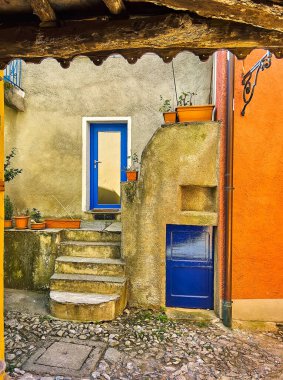 The tiny yard in a maze of medieval town streets with bright blue doors against the grey wall, Castello, Valsolda, Italy