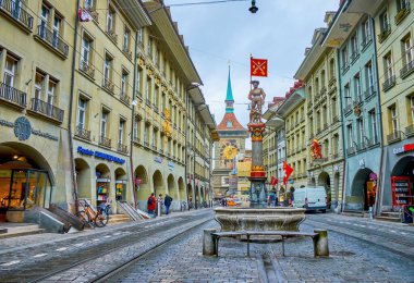 BERN, SWitzERLAND - 31 Mart 2022: Marktgasse caddesi boyunca yürüyün ve 31 Mart 'ta İsviçre' nin Bern kentinde, etrafındaki evlerin ortaçağ çeşmelerini ve manzaralı cephelerini geçin.