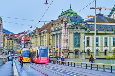 BERN, SWitzERLAND - 31 Mart 2022: Ortaçağ Altstadt bölgesinde Kornhausbrucke köprüsü boyunca iki renkli tramvay yolculuğu, 31 Mart 'ta İsviçre' nin Bern kentinde